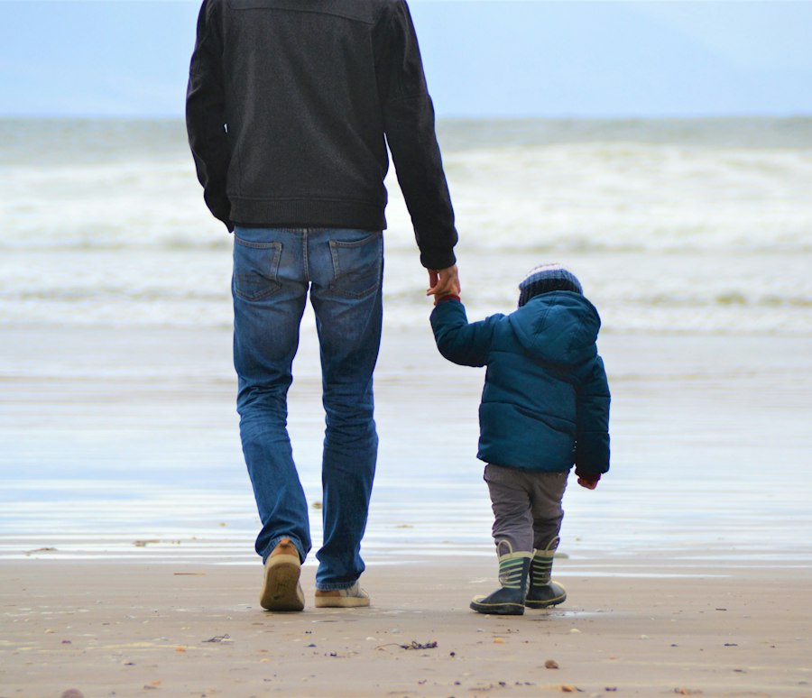 Pai caminhando de mãos dadas com o filho pequeno na praia